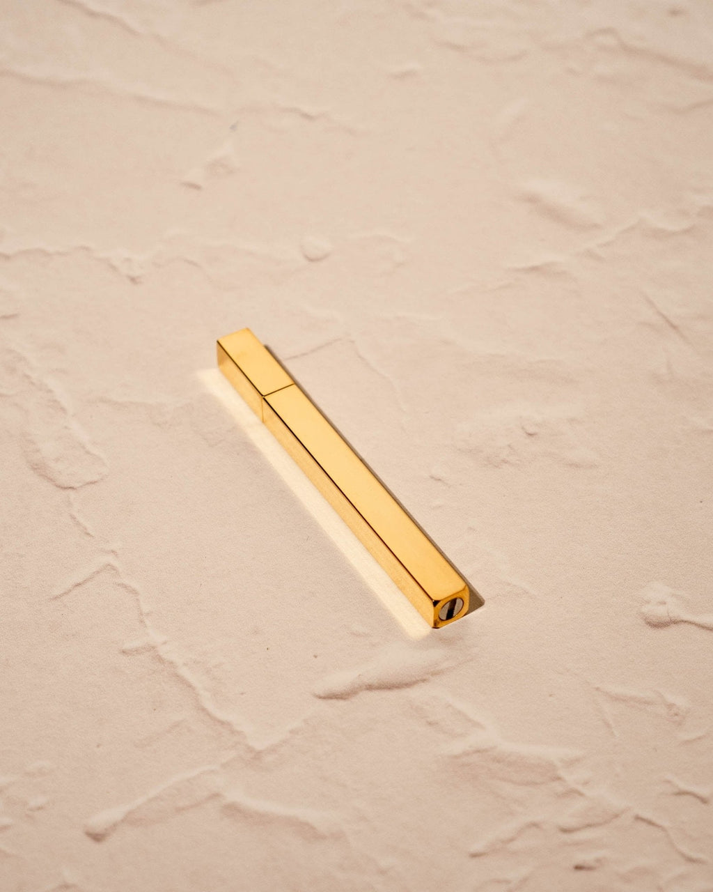 Gold Queue Lighter by Tsubota Pearl laying flat on textured beige surface