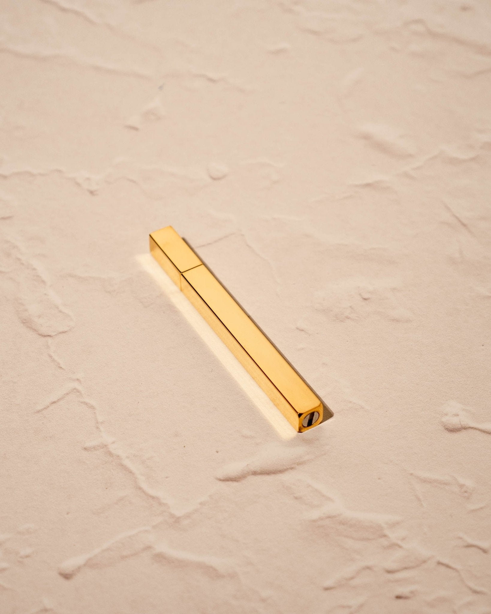 Gold Queue Lighter by Tsubota Pearl laying flat on textured beige surface