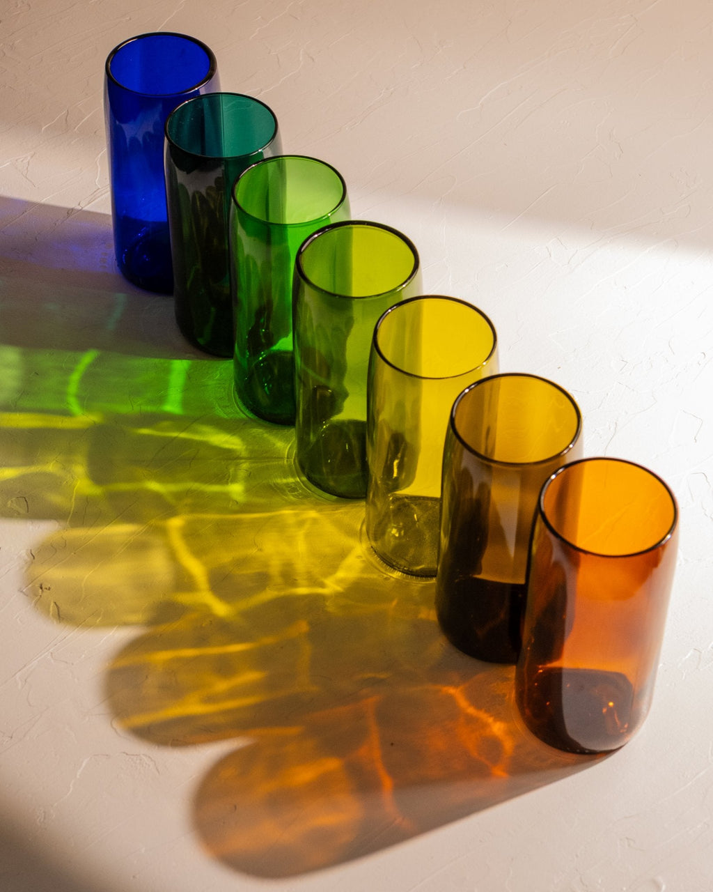 Recycled wine bottle incense vases in cobalt, teal, emerald, olive and amber glass casting colorful shadows