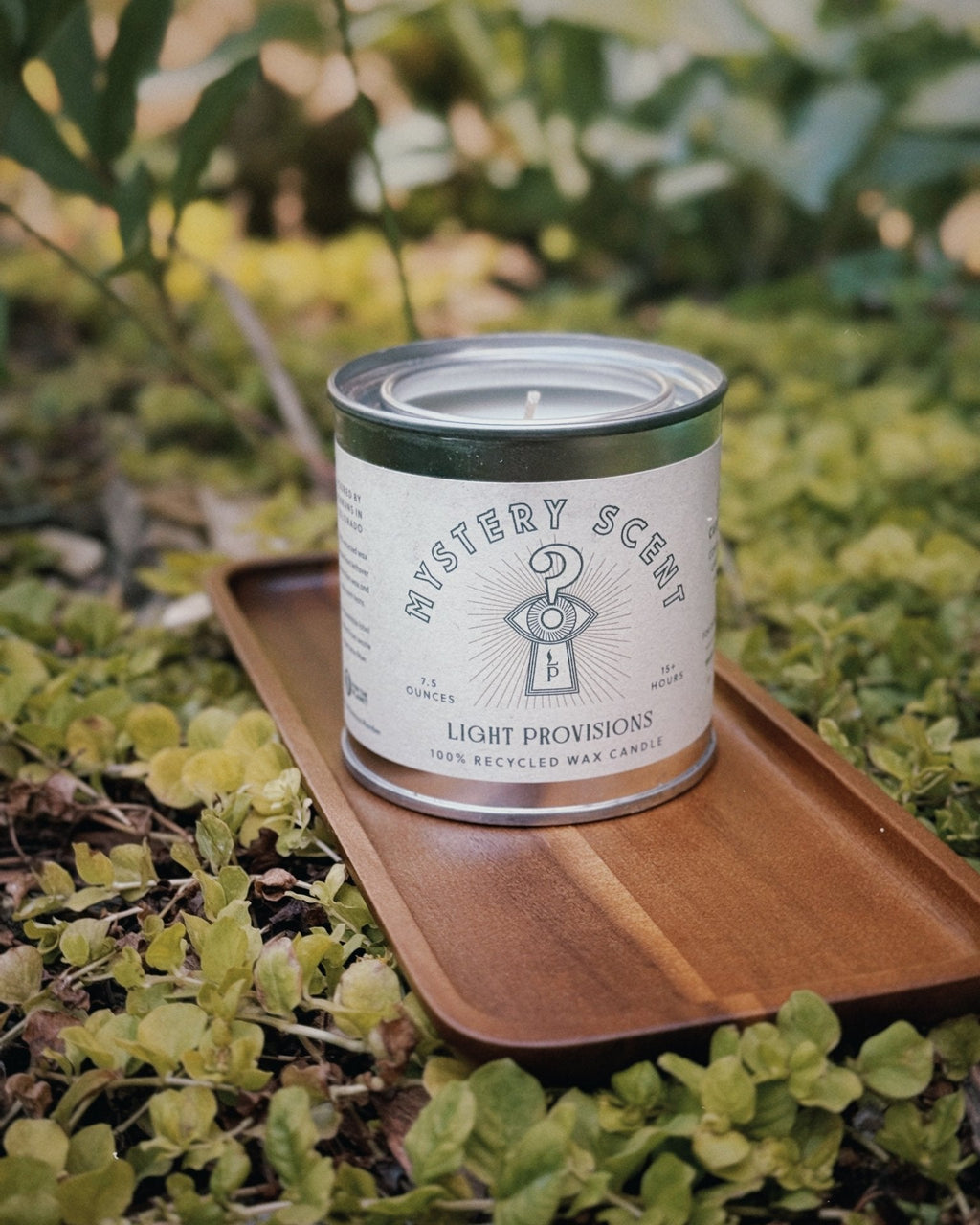 Recycled wax Mystery Candle in a reusable tin displayed on an acacia wood tray outdoors