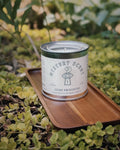 Recycled wax Mystery Candle in a reusable tin displayed on an acacia wood tray outdoors