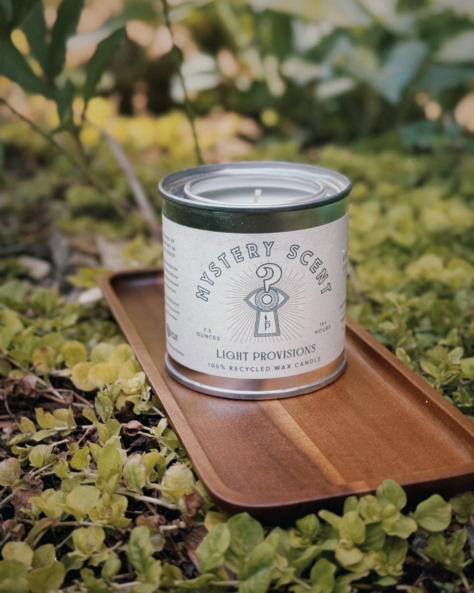 Recycled wax Mystery Candle in a reusable tin displayed on an acacia wood tray outdoors