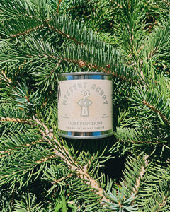 Candle labeled 'Mystery Scent' on a bed of green pine needles
