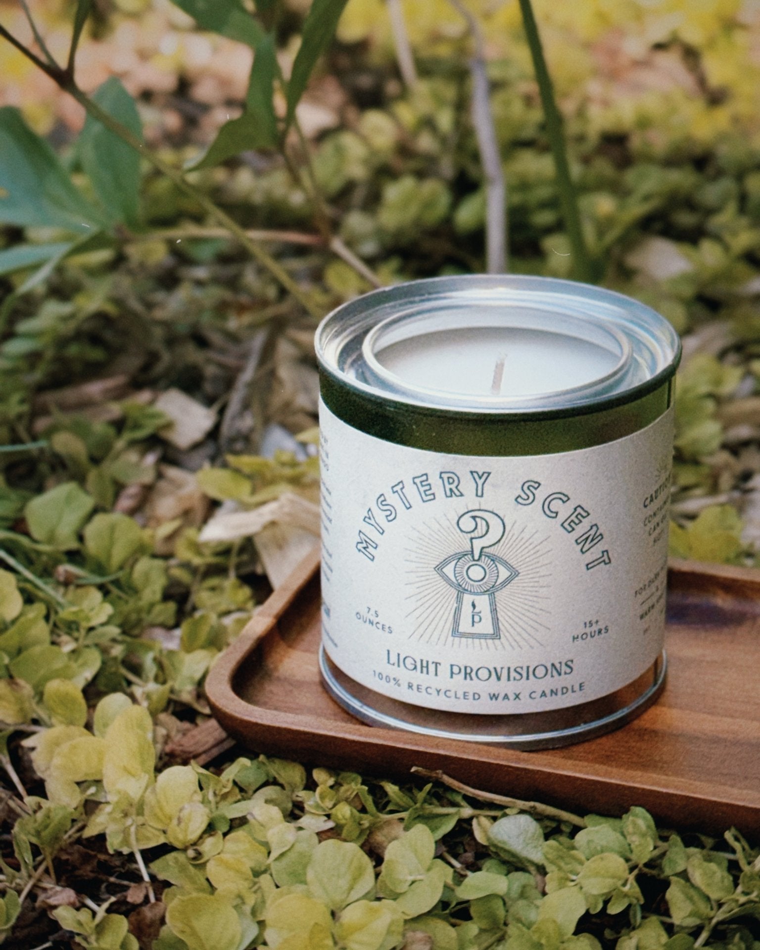 Recycled wax Mystery Candle surrounded by green ground cover on an acacia wood tray