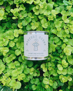 Candle labeled 'Mystery Scent' on a bed of green leaves