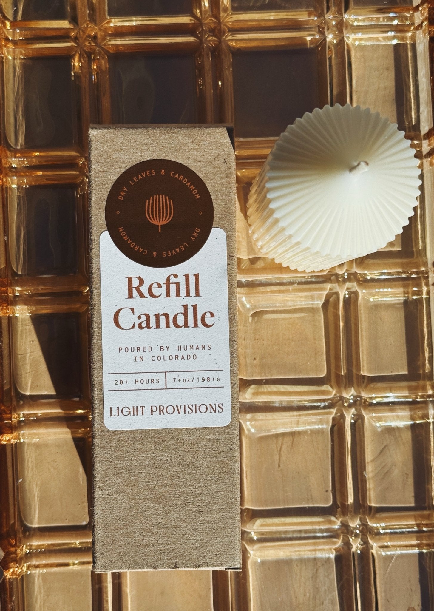 Dry Leaves & Cardamom Refill candle packaging with a candle on a textured gold surface