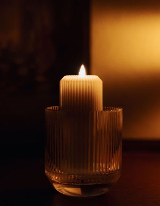 Low-burning refill candle with golden wax glow in ribbed signature glassware and warm amber light