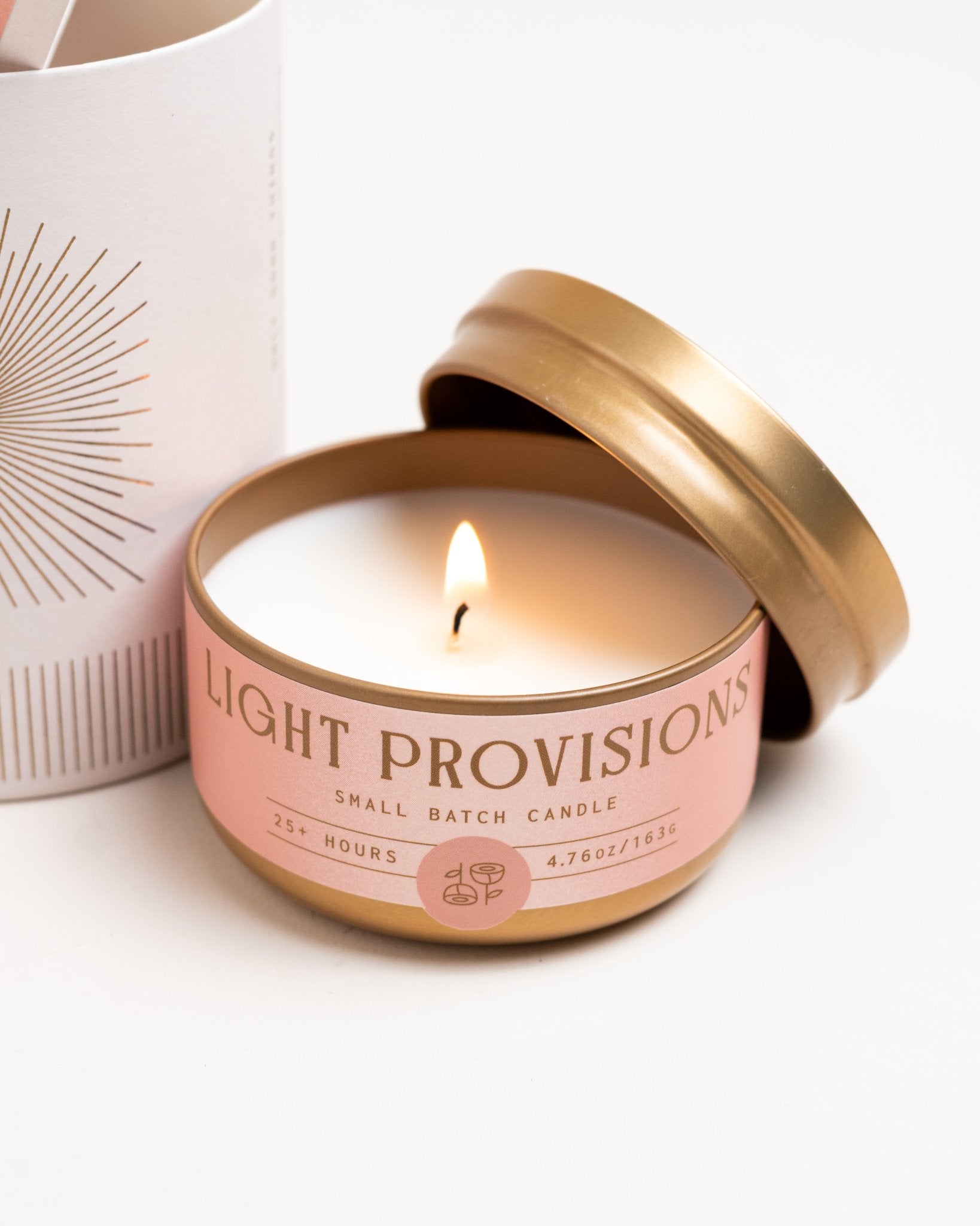 Rose & Fir candle tin burning with lid off next to tube packaging on white background
