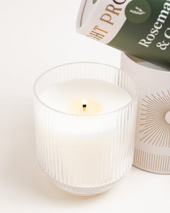 Macro of flame and melt pool in ribbed-glass Rosemary & Cedar tumbler candle, on white background.