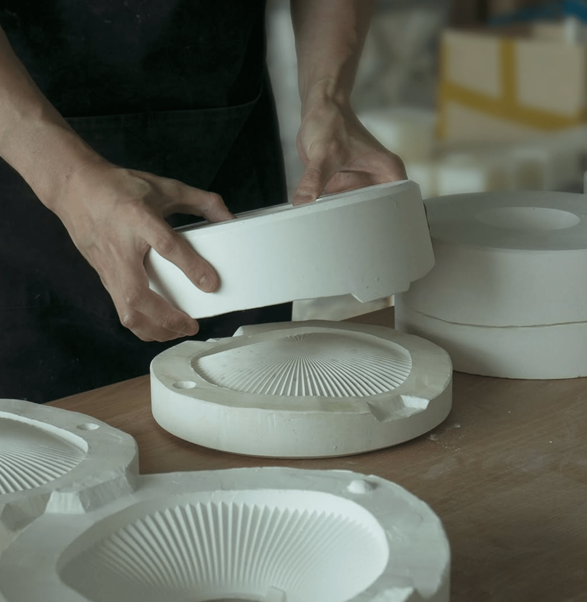 Hands assembling white ceramic incense holders with a mold on a worktable surrounded by other handmade components.