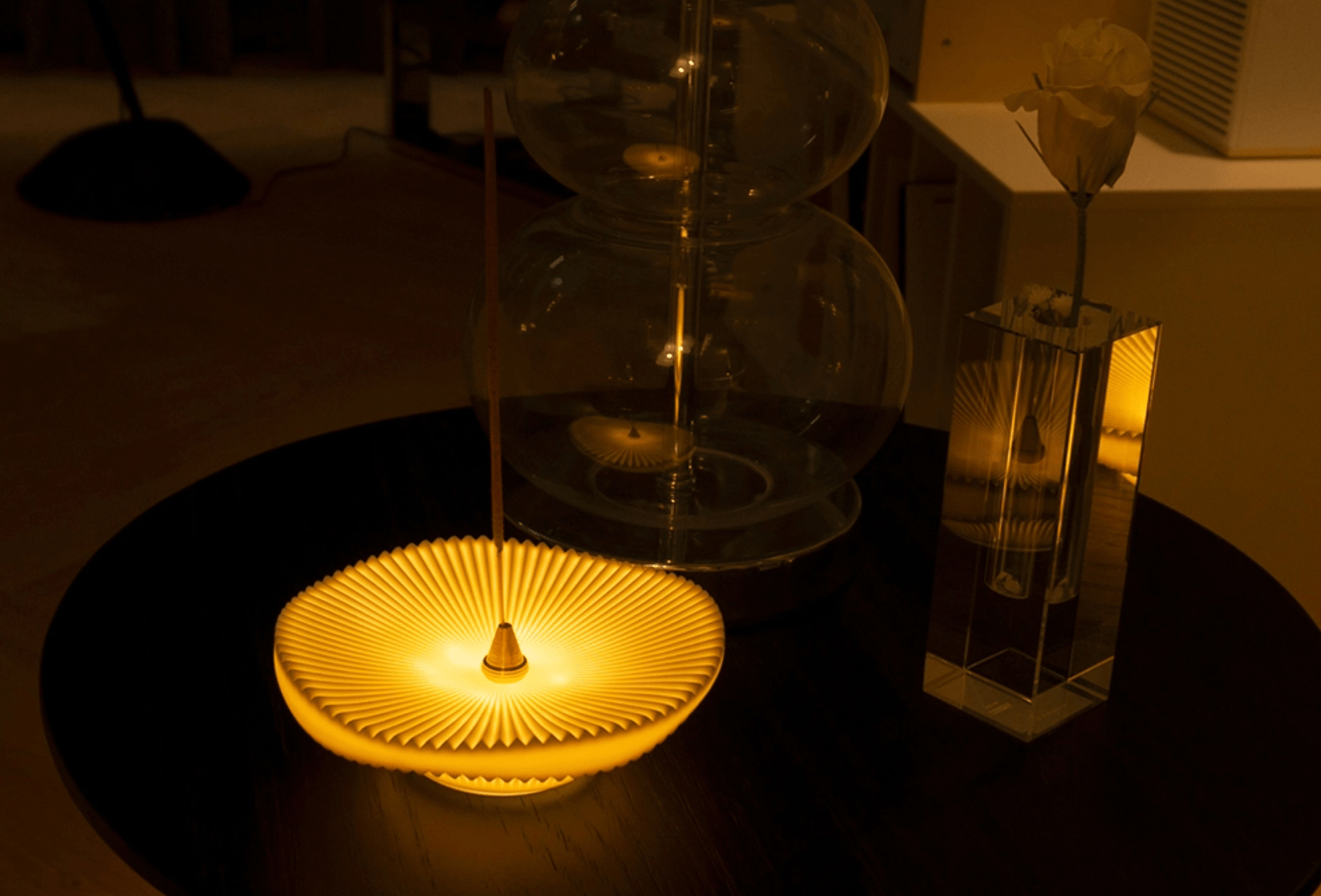 Close-up of illuminated ceramic incense holder on a tabletop beside glassware, creating a calm ambient scene.