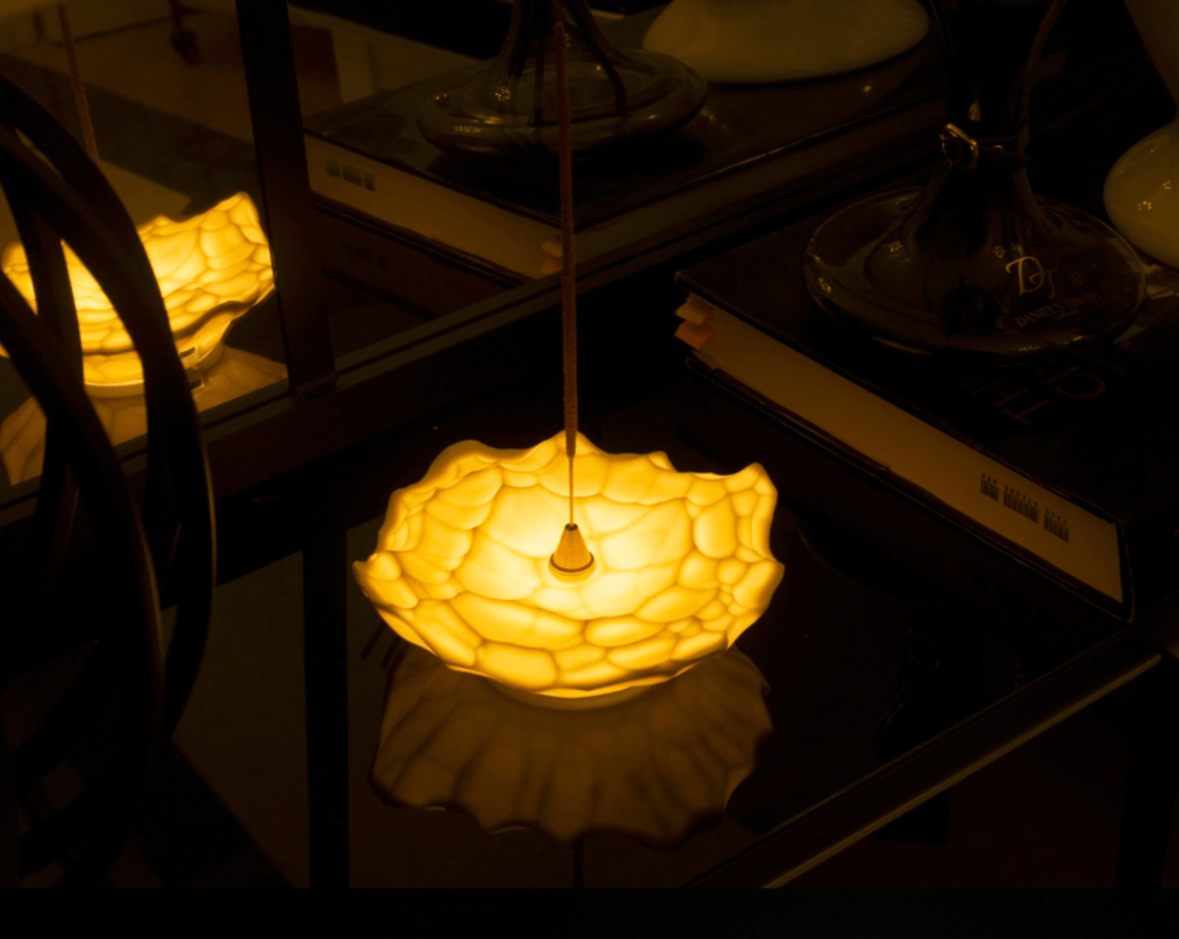 Ceramic incense holder glowing on a reflective tabletop surrounded by glass bottles and warm candlelight.
