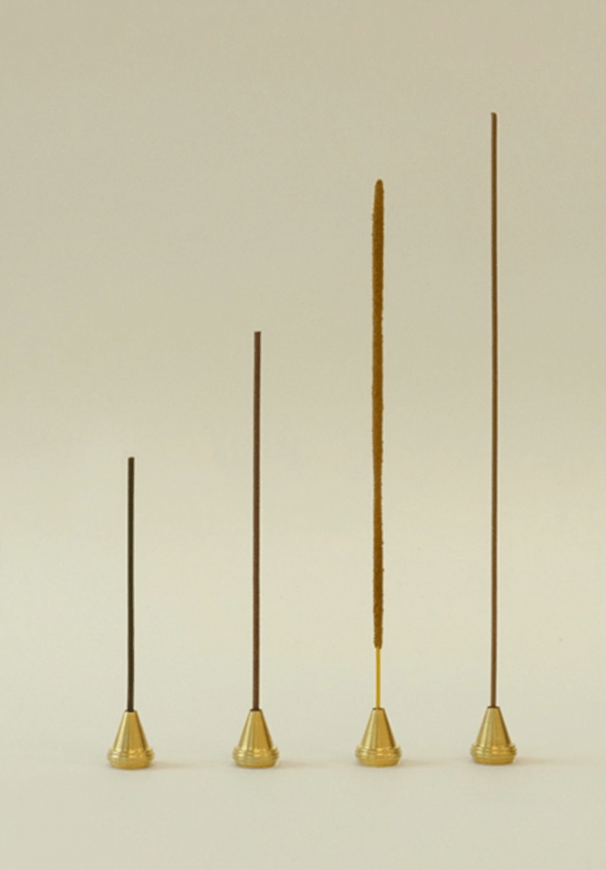 Four identical brass incense holders displayed with  incense sticks of varying lengths and types