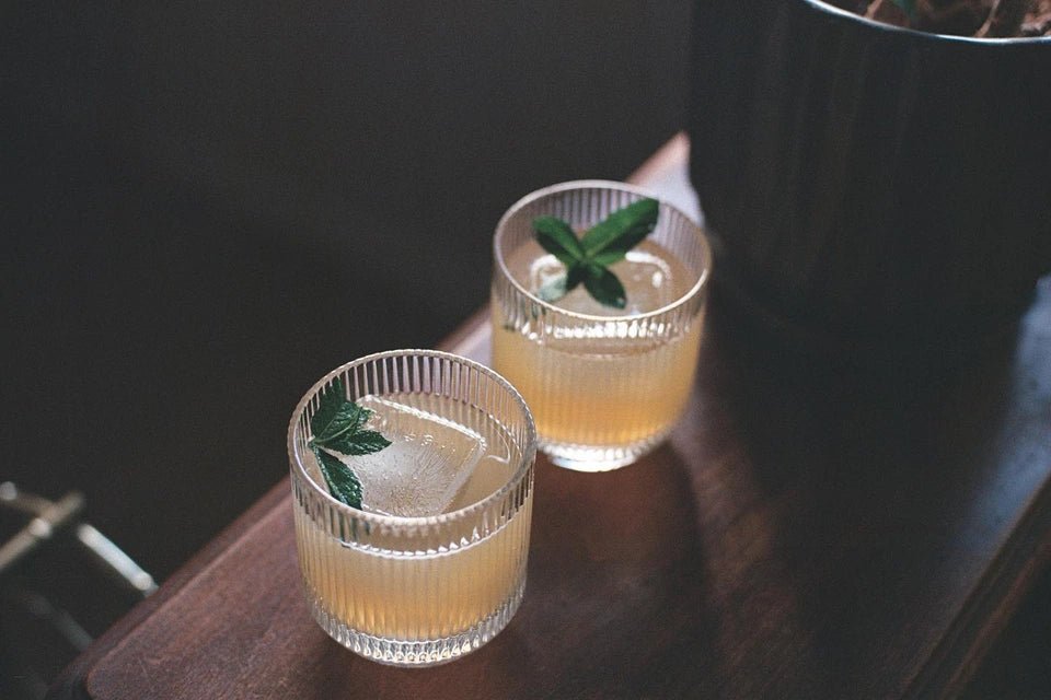 Hand-blown glassware with margarita cocktails and mint sprig styled on dark wooden surface