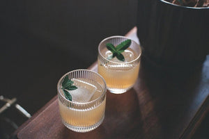 2 citrus cocktails side by side in signature rippled glassware, mint leaves and large clear ice cubes are present.  shot on 35mm film kodak portra