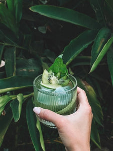 Close up of hand holding glassware with a tropical exotic cocktail and a leafy green background