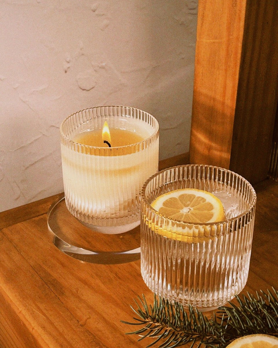 Hand-blown glassware containing soda and lemon peel with candle burning beside it
