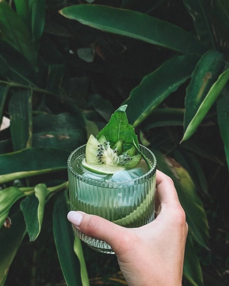 Bespoke hand-blown glassware holding green cocktail nestled among lush jungle plants