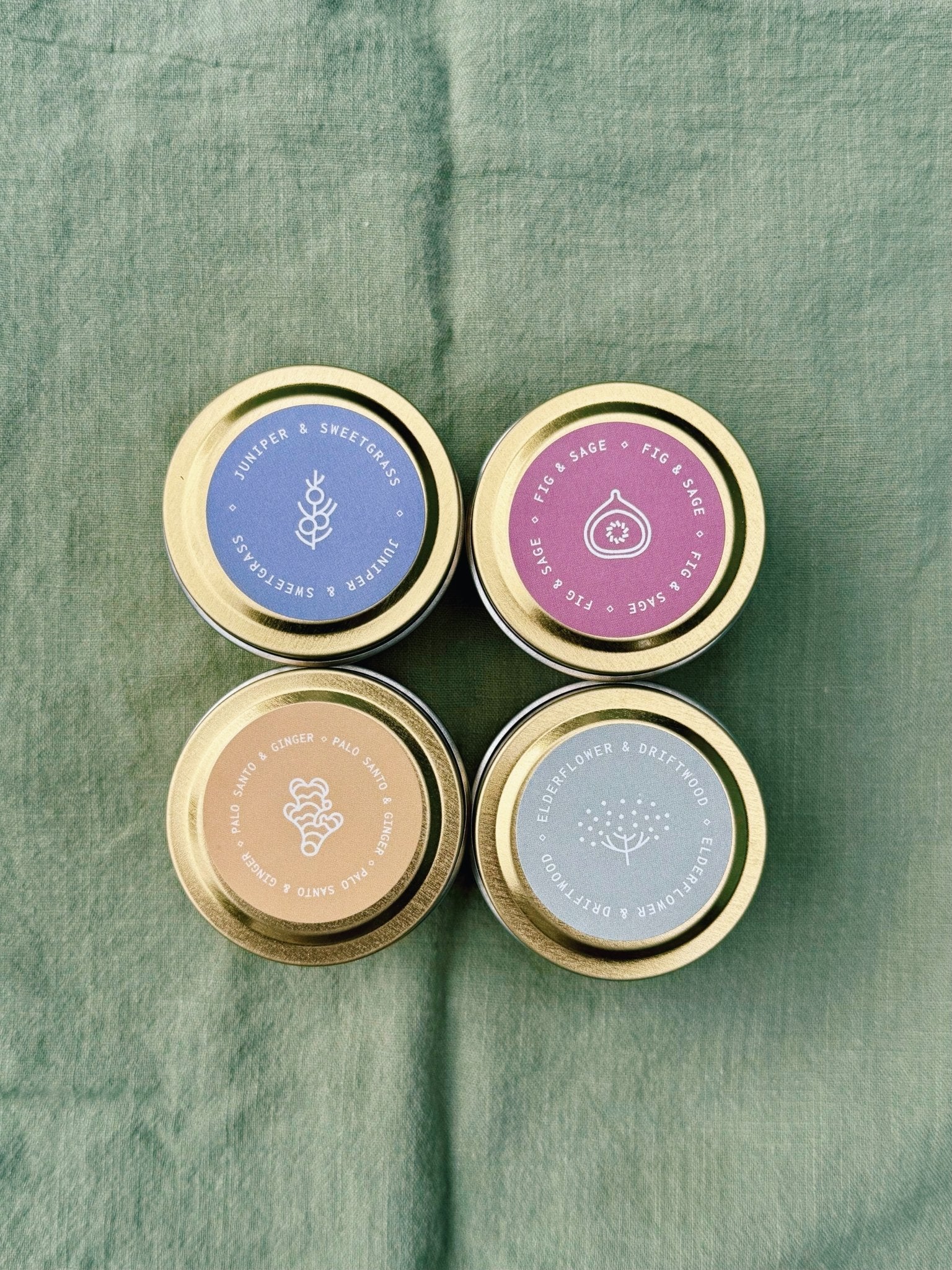 Four small Spring Candles with gold lids on a green fabric background