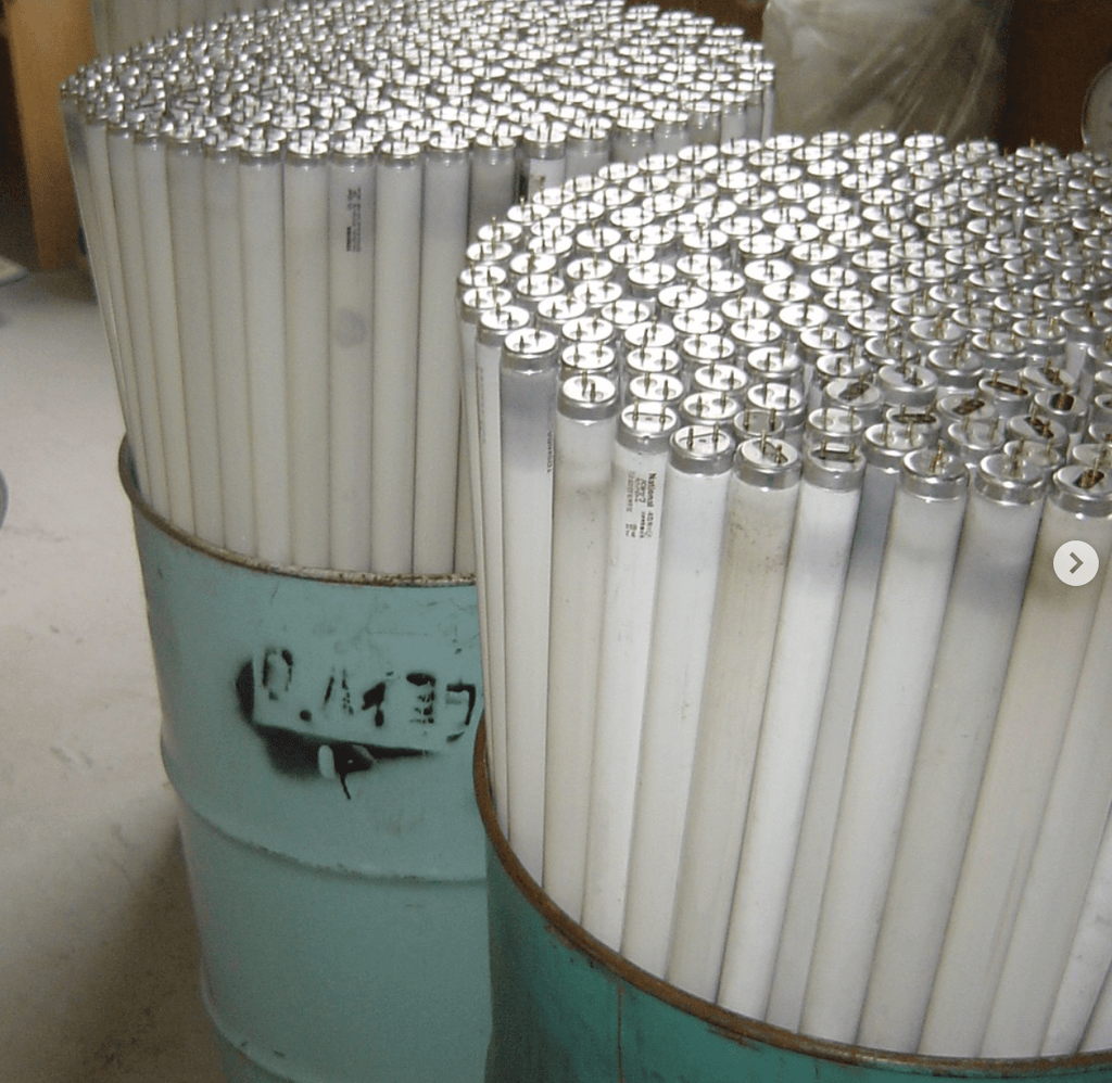 Stacks of used fluorescent lights ready for recycling in cylindrical containers on a concrete floor.