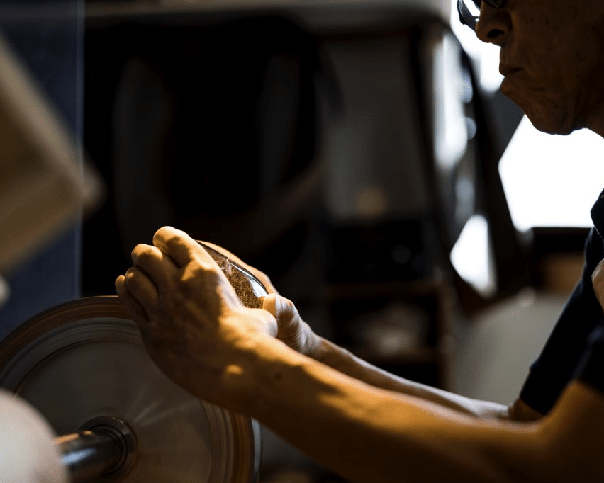 Person working with glass incense holder on a polishing wheel in a workshop setting