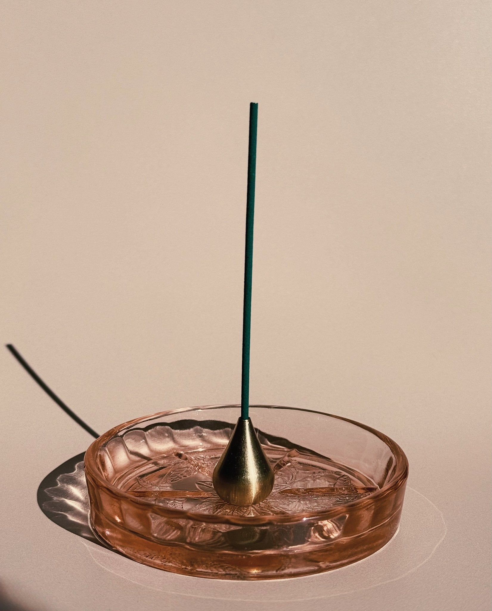 Incense stick in a vintage glass holder with a beige background and tall waterdrop incense holder