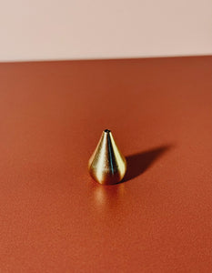Gold teardrop-shaped incense holder on a red surface with a pink background