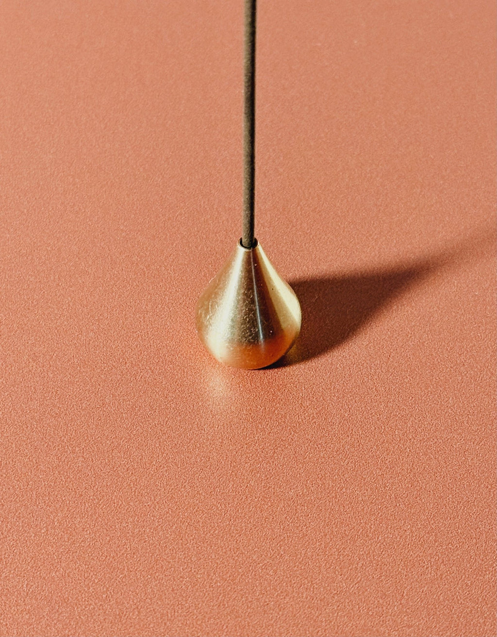 Gold teardrop-shaped incense holder holding japanese incense on a pink background