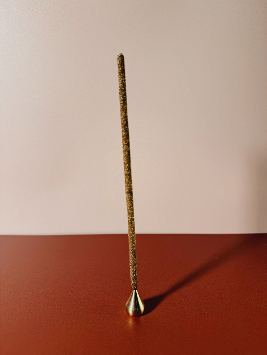 palo santo Incense stick in a brass teardrop holder on a red surface
