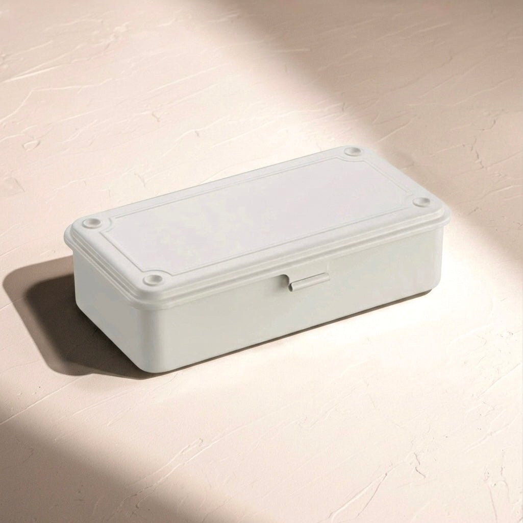 A rectangular white steel storage box with a hinged lid, shown on a textured beige surface with soft diagonal shadows.