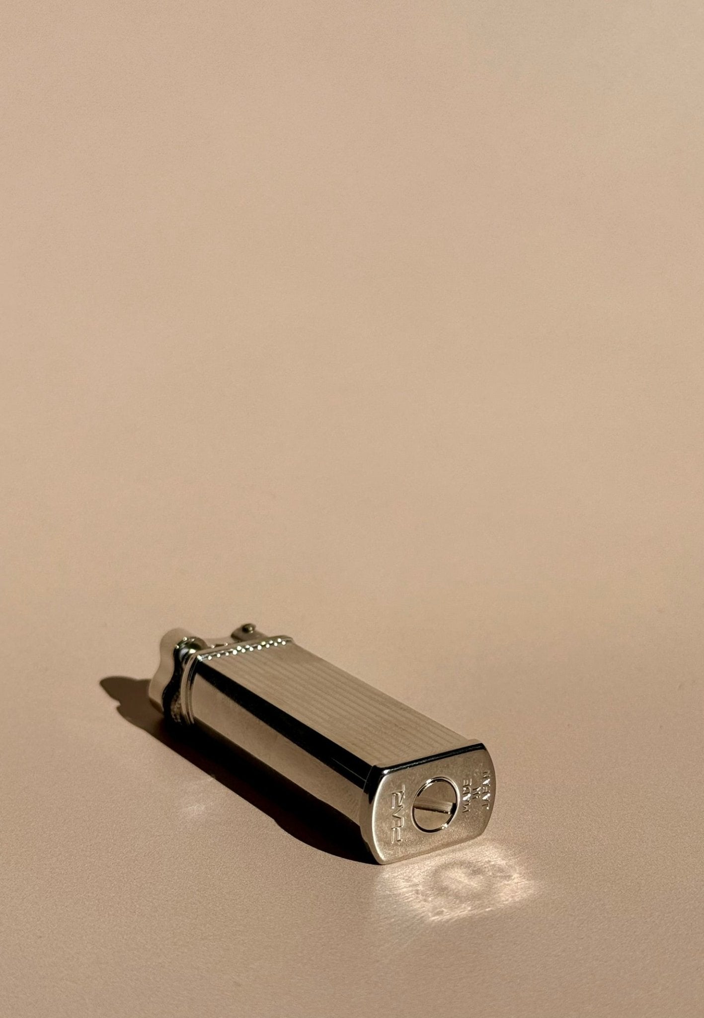 Tsubota Pearl Bolbo lighter shown lying flat with bottom screw exposed, photographed from above on a warm background.