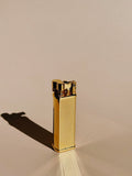Brass Striped Tsubota Pearl Bolbo lighter standing upright, photographed with shadow on a warm surface.