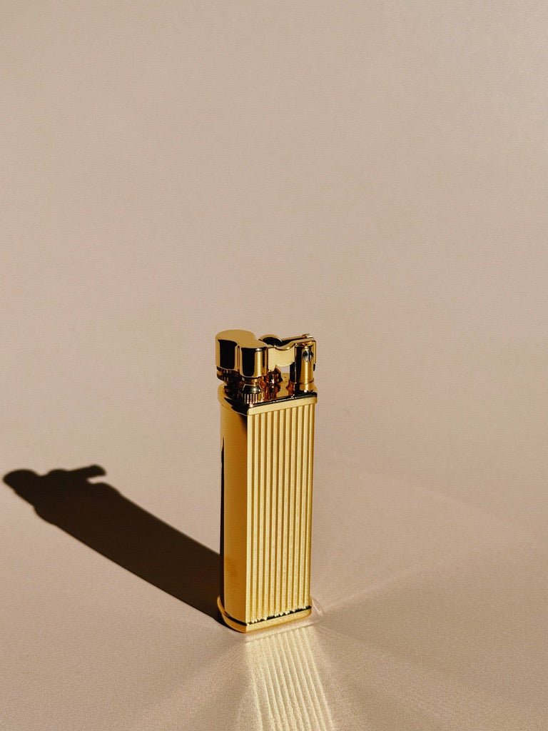Brass Striped Tsubota Pearl Bolbo lighter standing upright, photographed with shadow on a warm surface.