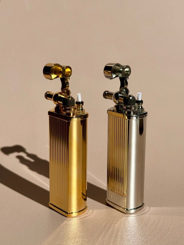 Tsubota Pearl Bolbo lighters in brass and silver finishes, photographed together on a warm tabletop.
