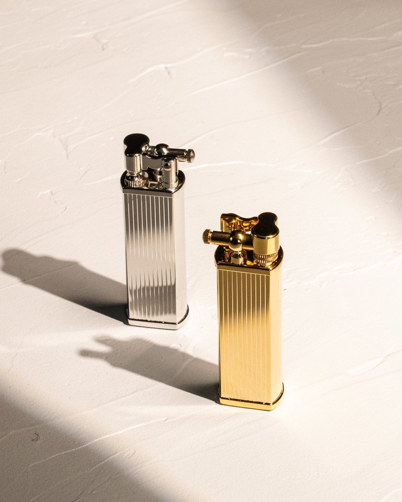 Two bolbo stripped tsubota pearl lighters, one silver and one gold, on a textured white surface.