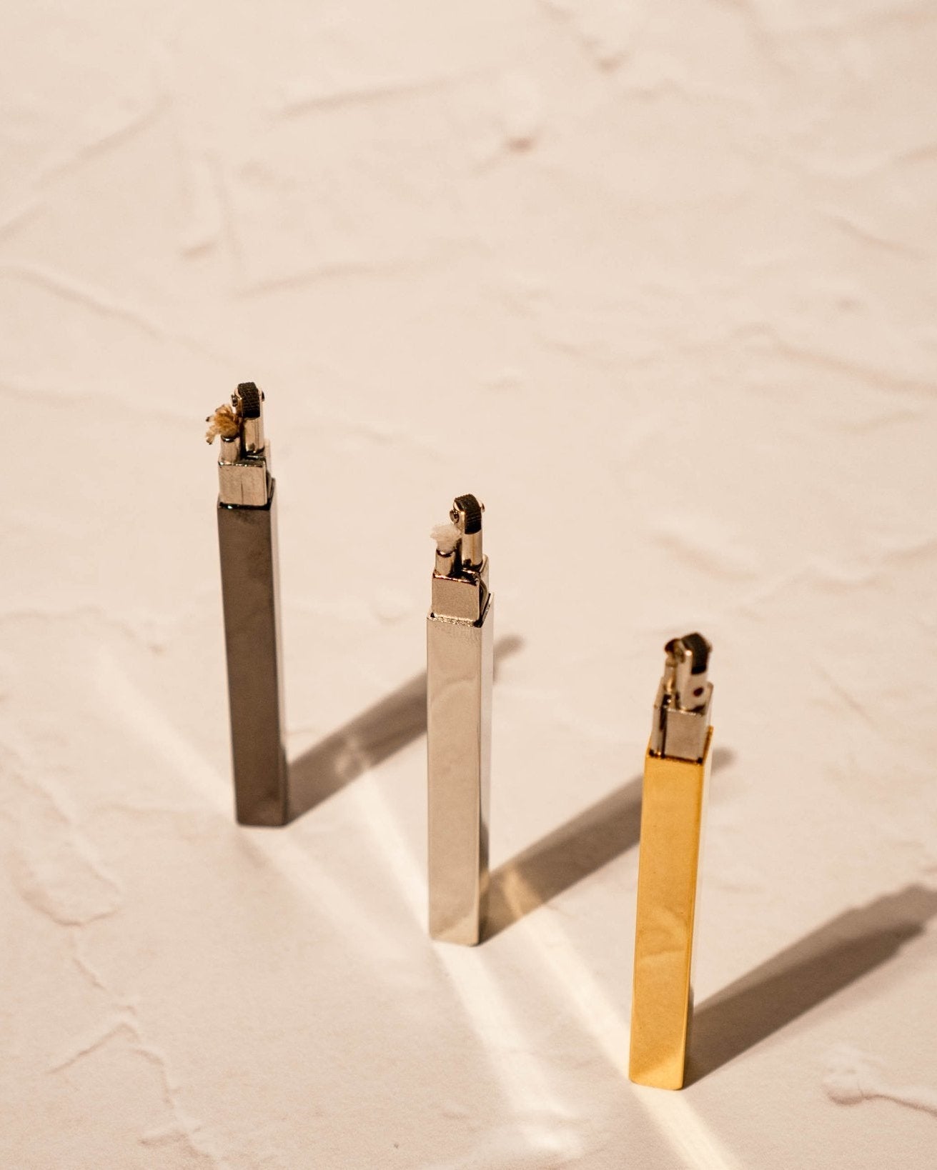 Three Queue lighters by Tsubota Pearl in black, silver, and gold