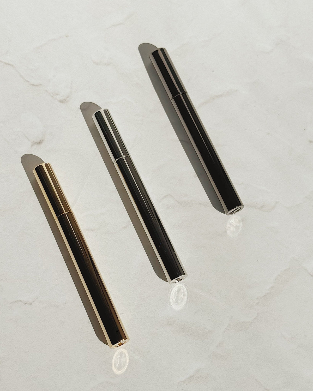 Gold, silver, and black Tsubota Pearl Sigaretta stick lighters arranged diagonally on a pale surface.