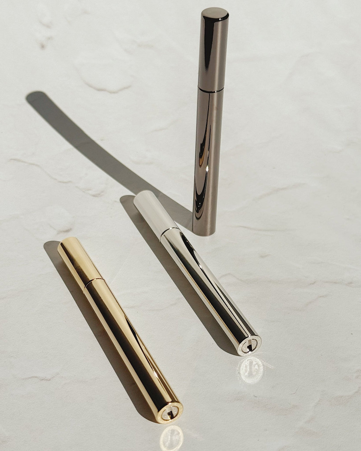 Tsubota Pearl Sigaretta stick lighters in gold, silver, and black, with one standing upright and two lying on a pale surface.