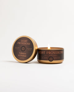 Open Light Provisions Tobacco & Walnut travel tin candle showing white wax, black label, and gold lid.
