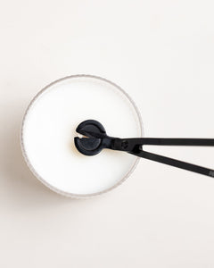 Top-down view of wick trimmer positioned above the center wick of a white candle.