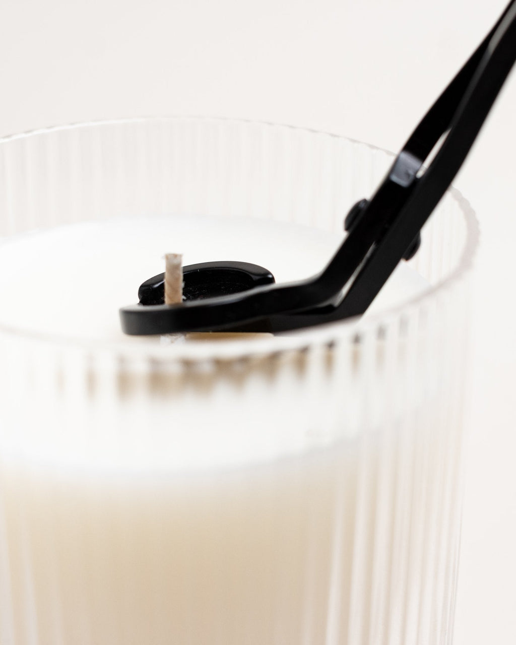 Black wick trimmer in use, trimming the wick of a white ribbed glass candle vessel.