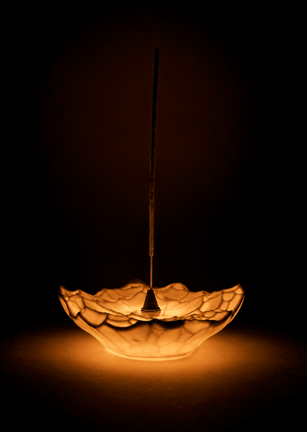 Gem sculptural incense holder light glowing warmly with a single incense stick against a dark background