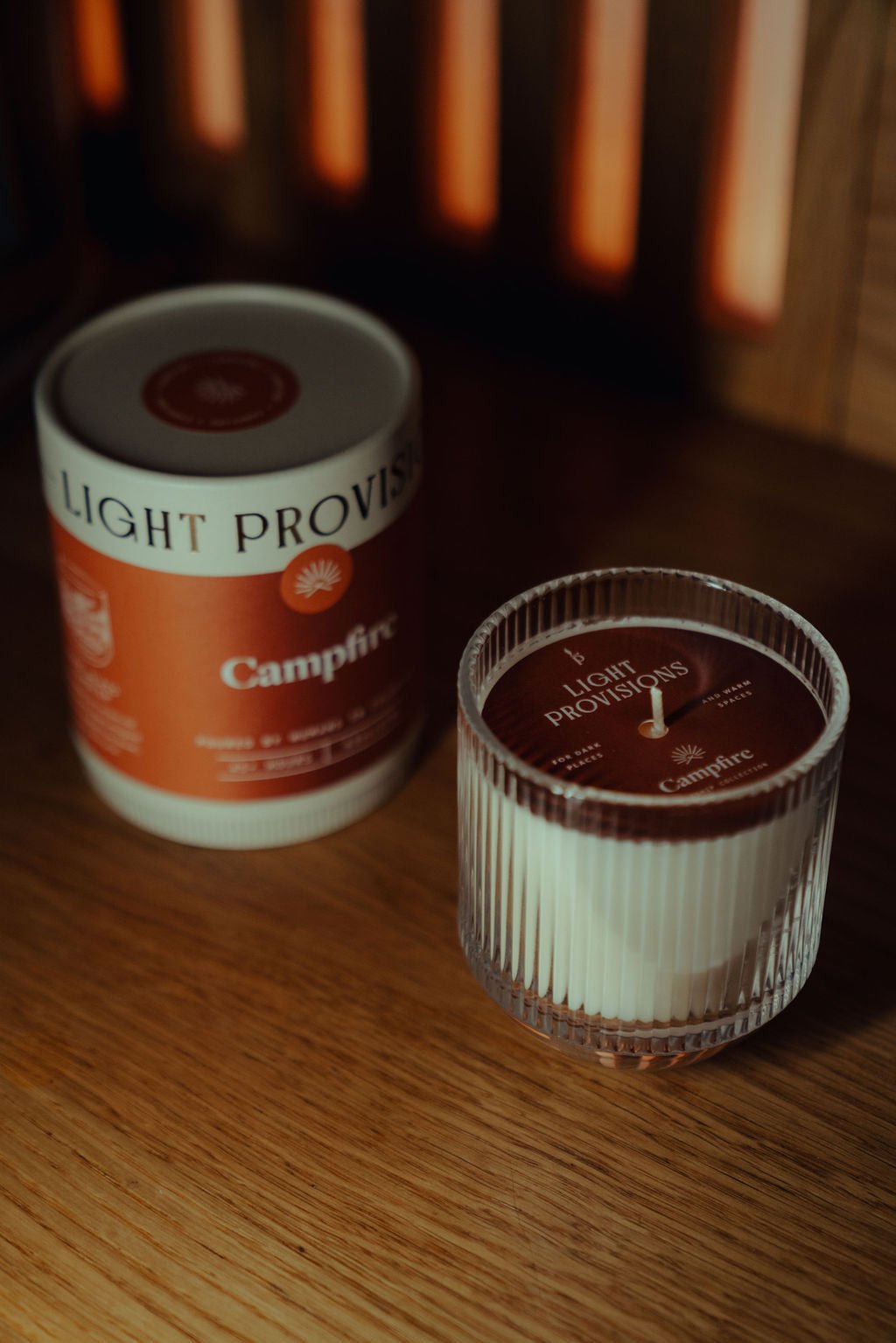 Campfire Candle in glass tumbler and travel tin side by side on wood surface