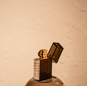 Closed black-striped Tsubota Pearl Hard Edge lighter standing upright with lid open. Brass gold surface of lighter is visible beneath polycarbonate shell