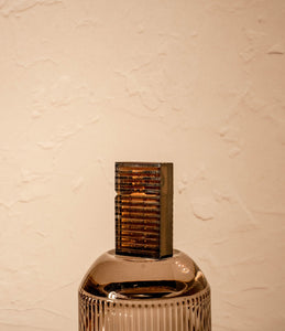 Closed black-striped Tsubota Pearl Hard Edge lighter standing upright on sunlit marble surface. Brass gold surface of lighter is visible beneath polycarbonate shell