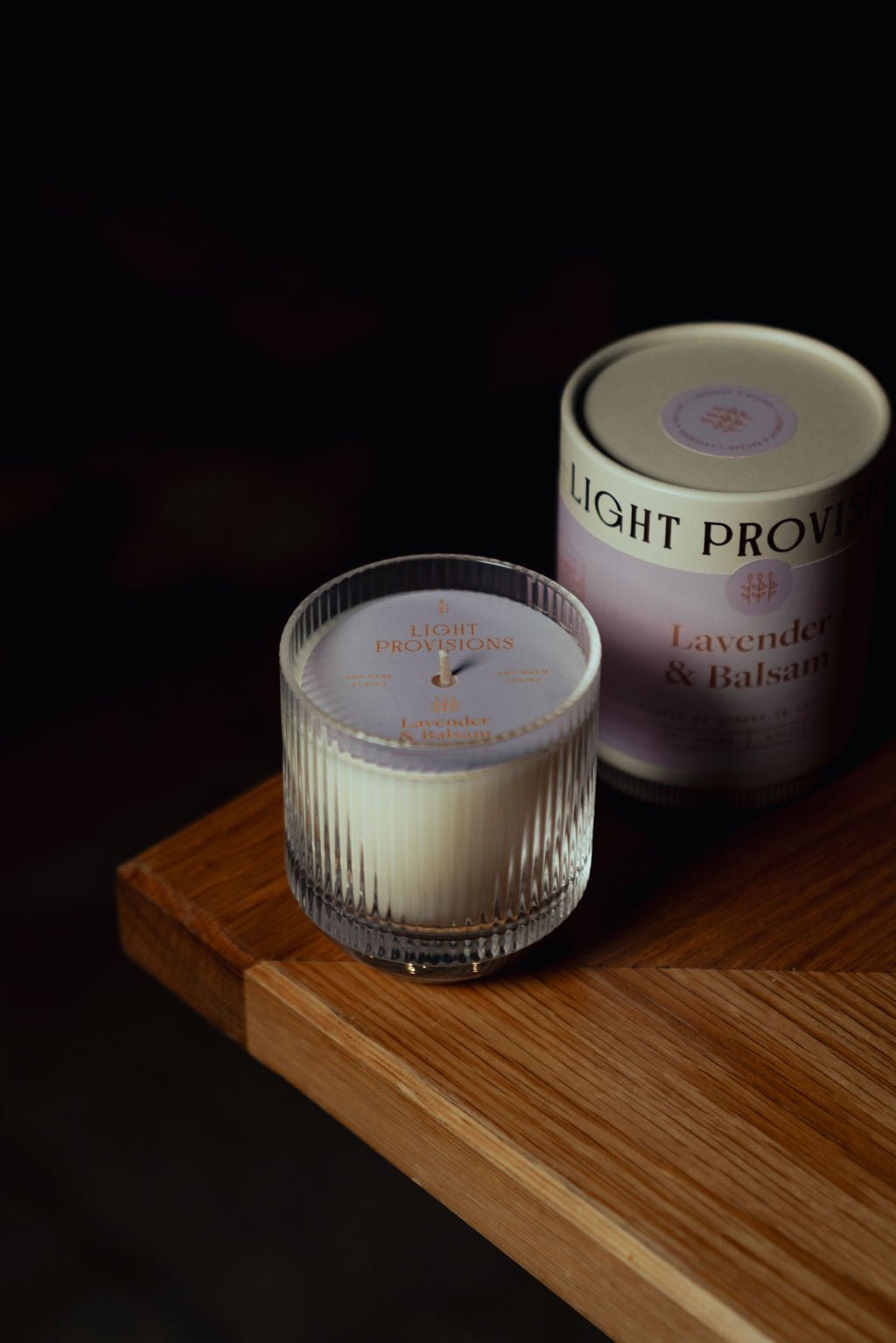 Lavender Balsam 9.5 oz glass tumbler and 4.75 oz travel tin candle styled together on wooden surface