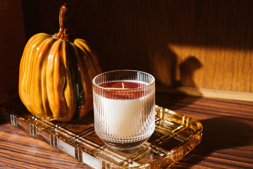 Pumpkin & Oud Wood Candle sitting on vintage amber tray with ceramic pumpkin in background