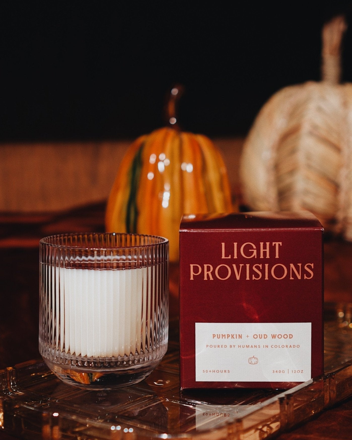 Pumpkin & Oud Wood Candle sitting on amber glass tray with Light Provisions packaging to right