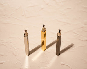 Tsubota Pearl Queue lighters in polished gold, silver, and black finish, photographed for Light Provisions against textured neutral background. Caps are removed showing flint wheel