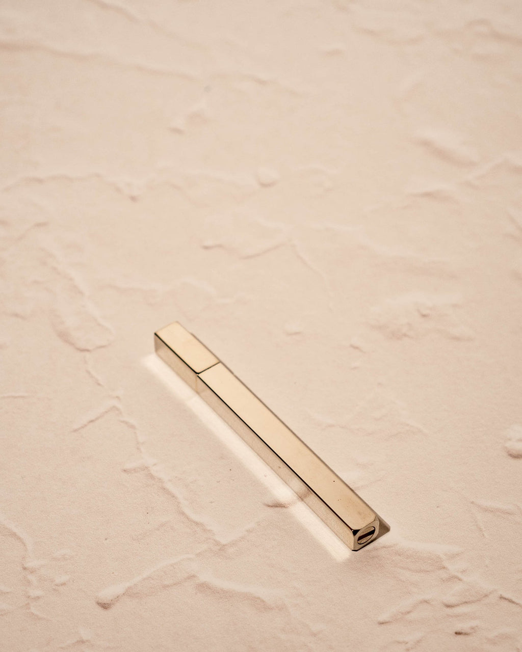 silver toned Queue Lighter by Tsubota Pearl in gold finish on textured beige surface